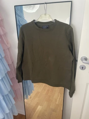 Olivgrön sweatshirt - Säljer en stilren olivgrön sweatshirt med rund halsringning och långa ärmar. Tröjan är i mjukt bomullsmaterial. 