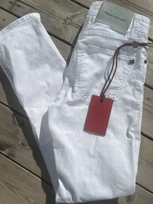 Vita jeans från Tramarossa - Snygga vita jeans från Tramarossa med klassisk femficksdesign och knappgylf. Jeansen har detaljer som märkets logga på bakfickan och insida, samt en röd tag. Perfekta för en fräsch och stilren look. OBS! En knapp har bytats ut ses i bild 2