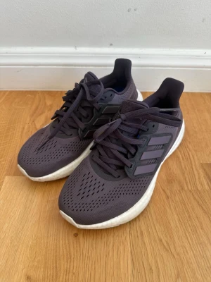 Lila Adidas sneakers med Boost-sula - Snygga lila Adidas sneakers med klassiska tre ränder på sidan och vit Boost-sula. Ovandelen är i ventilerande meshmaterial och skorna har svarta snören. Perfekta för en sportig och trendig look.