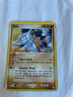 Onix Pokémonkort Team Rocket Returns - Säljer ett Onix Pokémonkort från Team Rocket Returns-serien, utgivet av Nintendo 2004. Kortet har gul ram, färgstark illustration av Onix och detaljerad text om attacker och effekter. Perfekt för samlare eller Pokémonfans.