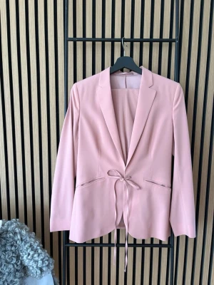 Rosa kostym från Filippa K - Rosa kostym från Filippa K. Kavaj med knytning framtill. Byxor i smalare modell. Kavaj i storlek: XS och byxa i storlek S. Tendens till mörk smuts i nacken. Använd två gånger. 