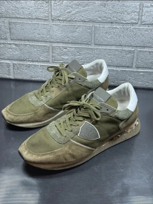 Olivgröna sneakers från Philippe Model - Säljer ett par Philippe Model Paris sneakers i storlek 45. Original (äkta).  Modellen har den klassiska “distressed/slitna” looken från början, men är även använda – se bilder för skick. Inga hål eller sprickor, bara normalt slitage.  Innermått ca 29 cm.  Snygga, bekväma och populära sneakers.  Pris: 1299 kr (kan diskuteras vid snabb affär) Skickas snabbt 📦