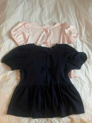 Mörkblå och rosa blus med puffärm och rosett - Söt blus med puffärmar och tre rosetter framtill. Tillverkad i mjukt tyg som känns skönt mot huden. Perfekt till sommaren 💗En för 80 kr eller båda för 150 kr (passar st S) 