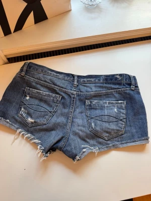 Blå slitna jeansshorts med fransar - Säljer ett par blå jeansshorts med slitna detaljer och fransig nederkant. Shortsens klassiska femficksdesign och låg midja ger en cool och avslappnad look. Perfekta för sommarens alla äventyr! Midjemått rakt över:40 cm💓