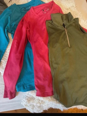 Ridtröjor st S - Två långärmade tröjor från TTL i blå och rosa samt en ärmlös olivgrön tröja från CRW  med halv dragkedja. Alla i mjukt, stretchigt material. Perfekta för ridning speciellt till sommaren och våren. Alla är i storlek S.