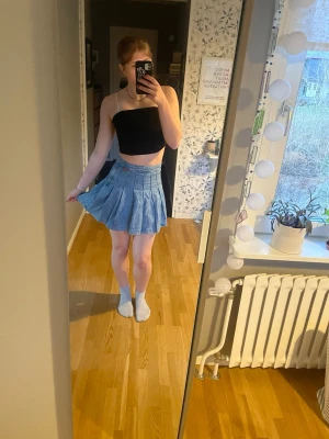 Ljusblå plisserad jeanskjol - Trendig ljusblå jeanskjol med plisserad design och hög midja. Kjolen är kort och har en klassisk denimlook som passar perfekt till sommarens outfits. 