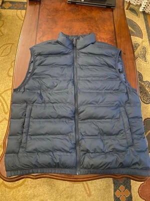 Mörkblå dunväst från Zara - Snygg mörkblå dunväst med hög krage och dragkedja framtill. Västen har quiltad design med horisontella sömmar och två sidofickor. Perfekt för lager-på-lager och håller dig varm under kyliga dagar. Materialet är lätt och isolerande. Använd 1 gång 