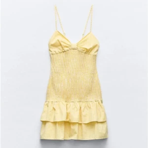 Gul kort klänning med volang från Zara  - Söt gul klänning med rutigt mönster, smala axelband och volang nertill. Klänningen har en rosett i ryggen och är perfekt för sommaren. Den är i storlek S men sitter som en xs 