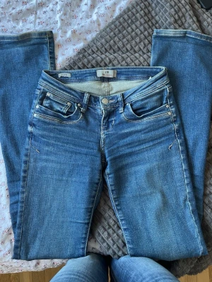 Blå jeans från LTB med vida ben - Storlek 24/36, ett par klassiska blå jeans från LTB med vida ben och fem fickor. Jeansen har snygga slitningar och ljus tvätt, samt detaljerade sömmar och läderpatch med logga bak. Perfekta för en avslappnad och trendig look.