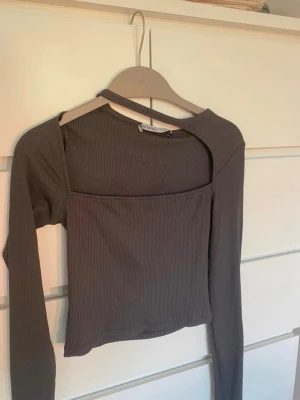 Ribbad grå långärmad topp Bershka - Trendig ribbad topp från Bershka i mörkgrått med lång ärm och unik cut out-detalj vid halsen. Toppen har en tight passform och är tillverkad i stretchigt material. Perfekt både till vardag och fest. Aldrig använd 