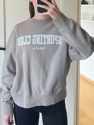 Beige sweatshirt från Björn Borg - Snygg beige sweatshirt från Björn Borg med trycket 'SPORTING CLUB' i vitt framtill. Tröjan har rund halsringning och avslappnad passform, perfekt för en chill och sportig stil. Tillverkad i mjukt bomullsmaterial som känns skönt mot huden.