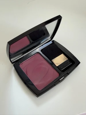Plommonfärgat blush från Lancôme - Snyggt plommonfärgat blush från Lancôme i en elegant svart dosa med spegel och tillhörande borste med gulddetalj. Rouget har en matt finish och kommer i en fyrkantig dosa som är perfekt att ha med i väskan.