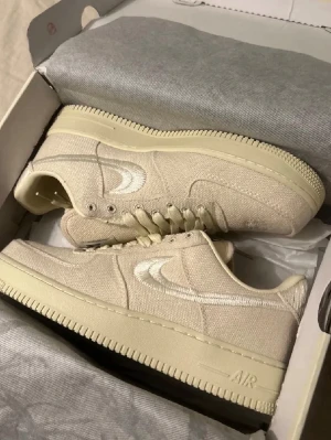 Beige AF1 sneakers - Snygga beige sneakers i canvasmaterial med ton-i-ton sula och broderad vit Swoosh på sidan. Klassisk låg modell med rund tå och snörning. Perfekta för dig som gillar stilrena och neutrala färger.