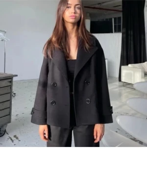 Marinblå dubbelknäppt kappa - Stilren (marinblå) kappa med dubbelknäppning och bred krage. Jackan har en boxig, något kortare passform och stora knappar framtill. Perfekt för dig som gillar en klassisk men modern look. (Den saknar en knapp men inget som är märkvärdigt)