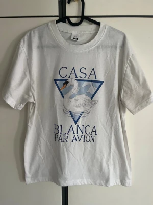 Casa Blanca t-shirt - Vit t-shirt från Casa Blanca med tryck av en svan och blå triangulär bakgrund samt texten 'Casa Blanca Par Avion' på framsidan. Klassisk rund hals och korta ärmar. Tillverkad i mjuk bomull för en skön känsla.