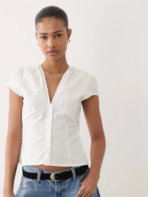 Ny Gina Tricot Vit blus med v-ringning och knappar - Stilren vit blus med djup v-ringning, knappar framtill och diskreta veck vid axlarna. Kortärmad modell i lätt och luftig bomull. Gina Tricot. Endast provad 