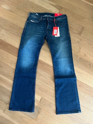 Blå bootcut jeans från Diesel - Snygga blå bootcut jeans från Diesel med klassisk femficksmodell och subtila slitningar framtill. Jeansen har normal midja och raka ben, tillverkade i ett mjukt denimtyg. Perfekta för en avslappnad och trendig look.