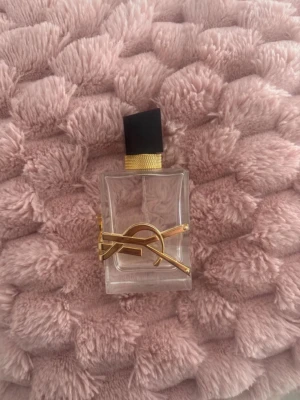 Yves Saint Laurent Libre parfym - Säljer en ikonisk Yves Saint Laurent Libre parfym. Flaskan är genomskinlig med guldiga detaljer och en svart, fyrkantig kork. Den har en lyxig och modern design med YSL-loggan i metall på framsidan. Perfekt för dig som gillar exklusiva dofter. Fins kvar lite om man vill testa inan man köper😍