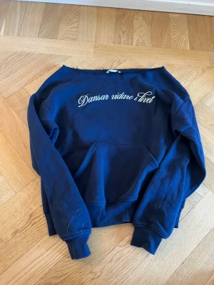Mörkblå hoodie Gina Tricot - Mörkblå hoodie från Gina Tricot med vit text 'Dansar vidare i livet' broderad på bröstet. Klassisk känguruficka framtill och ribbade muddar vid ärmar och nederkant. Tillverkad i mjukt bomullsmaterial för en skön och avslappnad look.
