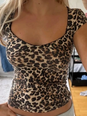 Leopardmönstrad topp med kort ärm - Snygg leopardmönstrad topp med korta ärmar och rundad urringning. Toppens material är stretchigt och följsamt, perfekt för dig som vill ha en trendig och bekväm look. Passar till både jeans och kjol för en cool outfit.(inte min bild)