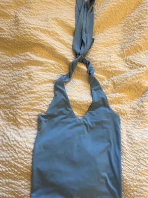 Ljusblå linnetopp - Supersöt ljusblå linnetopp med halterneck och knyt i nacken. Toppen har en djup v-ringning och är ärmlös, perfekt för varma dagar. Mjuk och lätt i materialet, passar till jeans eller kjol för en chill look.