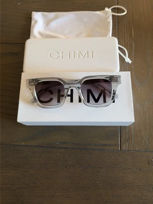 CHIMI transparenta solglasögon - Snygga solglasögon från CHIMI med transparent båge och mörka glas. Rektangulär form som ger en modern vibe. Kommer med originalfodral och tygpåse. Perfekta för att lyfta din stil under soliga dagar.