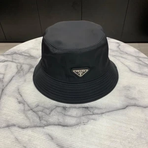 Svart bucket hat - Stilren svart bucket hat i nylon med klassisk siluett och det ikoniska metalltriangel-loggan framtill. Perfekt accessoar för att lyfta din streetwear-look och ge en exklusiv touch till outfiten.