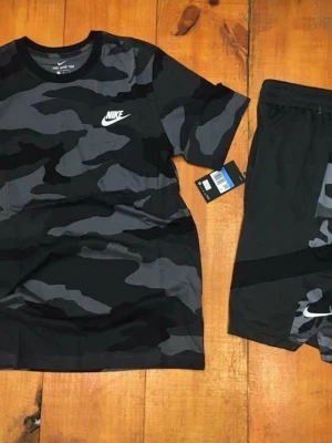 Nike camo set t-shirt och shorts - Säljer ett snyggt set från Nike med t-shirt och shorts i svart och grått camomönster. T-shirten har rund hals och Nike-logga på bröstet, shortsen har elastisk midja och logga på benet. Perfekt för träning eller chill.