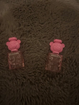 Moschino Toy 2 Bubble Gum parfym - Säljer två flaskor Moschino Toy 2 Bubble Gum parfym. Flaskorna är genomskinliga med rosa detaljer och har ett unikt lock i form av ett nallehuvud. Perfekt för dig som gillar lekfull och trendig design.