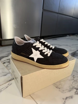 Svarta Golden Goose sneakers med stjärna - Snygga svarta sneakers från Golden Goose med vit stjärndetalj på sidan, vita skosnören och beige sula. Ovandelen är i textil och mocka för en cool och avslappnad look. Perfekta för dig som gillar streetstyle och vill sticka ut.