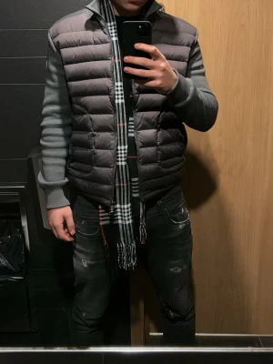 Moncler cardigan - Säljer en grå pufferjacka från Moncler med quiltad framsida och mjuka stickade ärmar. Jackan har två fickor med dragkedja och Moncler-logga på ärmen. Perfekt för dig som vill ha en snygg och bekväm jacka med streetkänsla. Storlek L men sitter som M