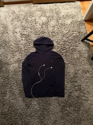 Mörkblå hoodie från Polo Ralph Lauren - Snygg mörkblå hoodie från Polo Ralph Lauren med klassisk huva och dragsko. Liten röd logga broderad på bröstet. Storleken är Medium. Hör av dig vid frågor!