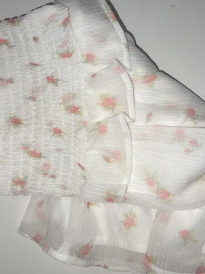 Blommig volangkjol finnes☺️ - Supersöt vit kortkjol från Gina Tricot med små rosa blommor och volangdetaljer. Kjolen har smock upptill och är gjord i ett lätt och luftigt material som passar perfekt för varma dagar. Den är i storlek 158/164 men passar XXS, xs & s också❣️Aldrig använd.