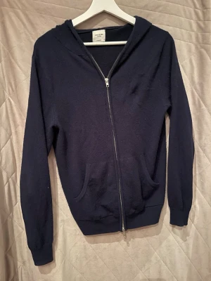Mörkblå John henric  - Säljer en mörkblå hoodie från John henric med dragkedja framtill och två fickor. Hoodien har ribbade muddar och en klassisk huva. Materialet är mjukt och bekvämt stickad Kashmir 