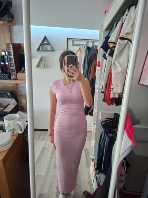 Ljusrosa långklänning med kort ärm - Säljer en ljusrosa långklänning med rund halsringning och korta ärmar. Klänningen har en figurnära passform och är tillverkad i ett mjukt, stretchigt material som sitter snyggt på kroppen. Perfekt för dig som gillar en enkel men stilren look. Aldrig använd.