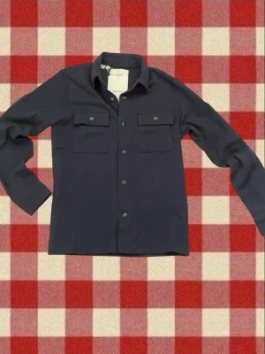Mörkblå overshirt  - Stilren mörkblå overshirt från selected med två bröstfickor med lock och knappar framtill. Klassisk krage och långa ärmar med knapp vid ärmslut. Perfekt lager-på-lager-plagg i mjukt material. Enkel och clean design som passar till mycket. Helt ny och inga defekter säljs för att köpte fel storlek