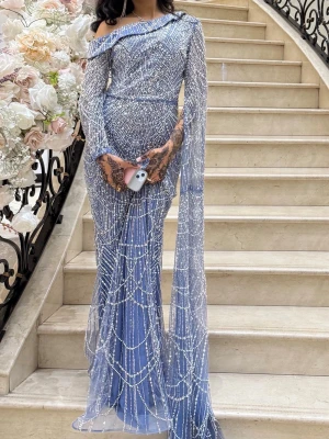 Elegant blå balklänning/festklänning - Magisk blå långklänning med glittrigt mönster och pärldetaljer. Klänningen har oneshoulder-design, lång ärm och ett elegant släp. Figurnära passform och skimrande material gör den perfekt för bal eller fest.