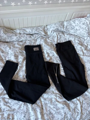 Svarta leggings med hög midja - Ett par för 50kr Två par svarta leggings med hög midja och stretchigt material. Ena paret har dragkedja framtill och det andra har en bred resår i midjan med en liten logga. Perfekta för en avslappnad och trendig look. Perfekt för att ha under stövlar 👢!!!
