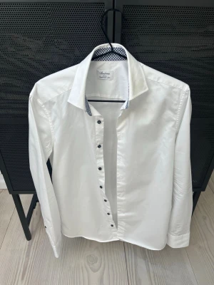  Stenströms slimline - Klassisk vit skjorta från Stenströms i slimline-modell. Skjortan har blåvitt mönstrat tyg på insidan av kragen och knappslån, samt svarta knappar. Tillverkad i exklusiv twofold super cotton för en lyxig känsla. Perfekt för en clean och stilren look.