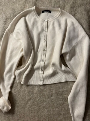 Vit ribbad kofta från Gina Tricot - Snygg vit kofta från Gina Tricot med rund halsringning och knappar framtill. Koftan har ribbade muddar och är tillverkad i ett mjukt, stickat material. Perfekt att slänga över en topp för en clean look.