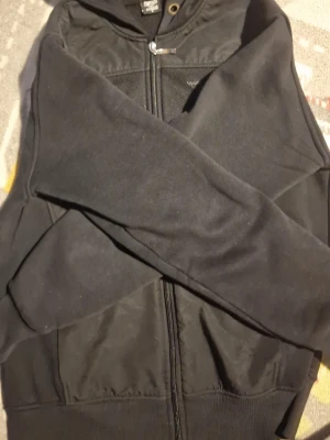 Svart hoodie från Emporio Armani - Snygg svart hoodie från Emporio Armani med dragkedja framtill och huva med snörning. Tillverkad i mjukt material och har ribbade muddar vid ärmslut och nederkant. Perfekt för en avslappnad och stilren look. Det står S men funkar även bra för M. Priset är diskuterbart