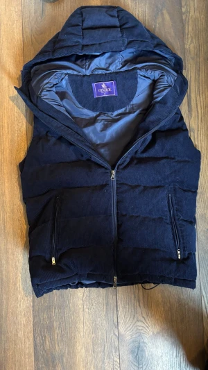 Mörkblå dunväst från Vonroe - Snygg mörkblå dunväst från Vonroe med huva och dragkedja framtill. Västen har två praktiska fickor med dragkedja och är tillverkad i ett mjukt manchestertyg. Perfekt för lager på lager och ger en cool look till din outfit.