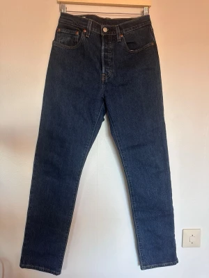 Levi's mörkblå raka jeans - Säljer ett par klassiska mörkblå jeans från Levi's med rak passform och fem fickor. Jeansen har hög midja och är tillverkade i slitstark denim. Ikonisk läderpatch på bakfickan och röda Levi's-tag. Perfekt för dig som gillar tidlös stil.