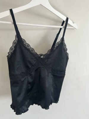 Svart festtopp med spets - En fin svart festtopp i silkesmaterial och spetsdetaljer. Aldrig använd