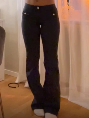 Svarta bootcut jeans med knappar - Säljer ett par svarta bootcut jeans med snygga silverfärgade knappar framtill och vid fickorna. Jeansen har låg midja och utsvängda ben, vilket ger en trendig siluett. Perfekta för dig som gillar en stilren och modern look.