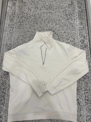 Vit halfzip hoodie från Zara - Säljer en stilren vit hoodie från Zara med halfzip-dragkedja och hög krage. Tillverkad i mjukt bomullsmaterial och har långa ärmar samt ribbade muddar. Perfekt för en clean och avslappnad look.