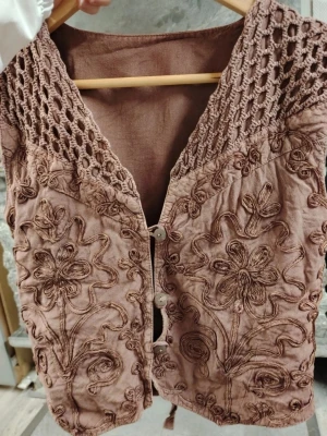 Brun virkad väst med blommönster - vintage! ❤️  - Unik brun väst med virkade detaljer upptill och broderade blommor över hela framsidan. Västen har knäppning framtill med två knappar och är tillverkad i ett mjukt tyg som ger en bohemisk känsla❤️ Perfekt för att lyfta vilken outfit som helst🤩 