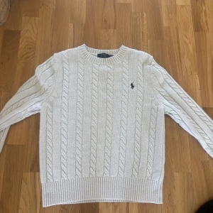Vit kabelstickad tröja Polo Ralph Lauren - Säljer en vit kabelstickad tröja från Polo Ralph Lauren med klassisk rund hals och ribbade muddar. Tröjan har svart RL logga, stolek S men passar även XS