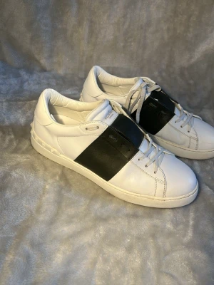 Valentino vita sneakers med svart band - Snygga vita sneakers från Valentino med ett brett svart band över mitten. Skorna är som nya och väldigt fräscha 🙌 FRAKTAR INOM 24 H.          Vi checkar noga igenom att skorna är äkta så man inte behöver oroa sig om skorna är fejk 🙌🤝📦