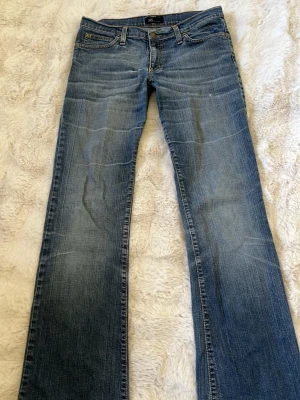 Blå bootcut jeans med slitningar - Säljer ett par klassiska blå bootcut jeans med snygga slitningar och lätt tvättad look. Jeansen har fem fickor och normal midja. Perfekta för dig som gillar en avslappnad men ändå trendig stil.